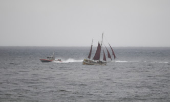 一艘美国海岸警卫队的小船正进行搜寻工作从经过的帆船附近驶过。AP图片