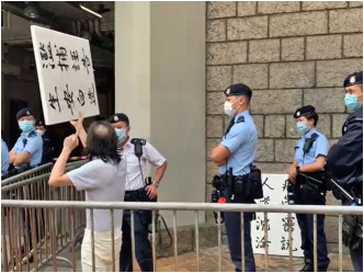 高院庭外一位男子高舉兩塊寫有「人道沉淪 疲勞審訊」、「舉證未有 人已先囚」的發泡膠牌。