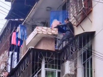 工人将老妇抱住，助爬回阳台。影片截图