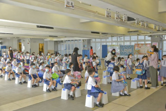 在老師安排下，小學生相隔一定距離坐好，等候上課室。
