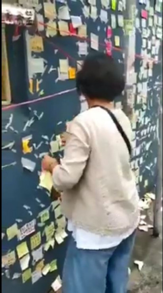 一名中年女子正撕走貼在牆上的紙張。影片截圖