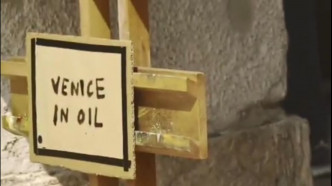 攤販左下角擺著一個標示寫著：Venice in Oil（威尼斯在油污中）。影片截圖