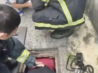 其中一名消防员将整个上半身钻进坑渠内，从里面协助女婴把脚抽出。网图