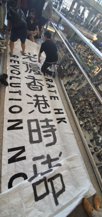离境大堂外的行人天桥站上，有人放下一块写有「光复香港时代革命」的直幡。