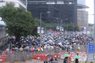 现场不时下骤雨，示威者手持雨伞，坚持留守现场。