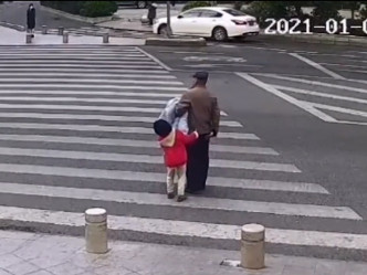孙女在马路中央尝试拉住爷爷的衣服阻止。影片截图