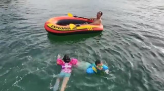 三位小朋友围住爸爸架艇游水。
