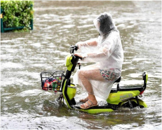 市民在街头积水路段骑车冒雨出行。网图