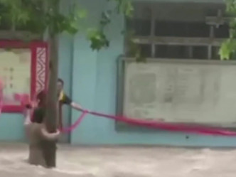 路人用广告条幅营救被困洪水的女子。网图