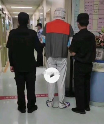 片中男子被兩名警員押往看醫生，腳上戴上腳鐐及笠頭套。