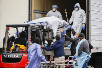 穿上保护装束的人员把一具具遗体抬上冷藏卡车运走。AP