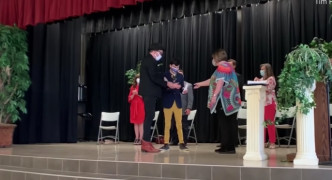 Odin在爸爸陪同下行上高中毕业礼的舞台，亲自接过毕业证书。 网图