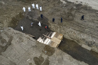 多名穿上防護衣的人員在島上挖坑埋葬屍體。 AP