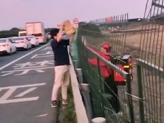 一名麥當勞外賣員隔著欄杆，正在把餐點拿給高速公路上的一名男子。影片截圖