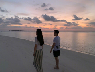 两人在夕阳美景下漫步沙滩。