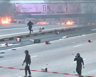 蒙面黑衣人在红隧九龙出入口焚烧杂物。港台新闻截图