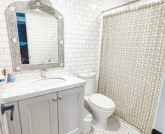 浴室设计具时尚感，墙壁铺上白色瓷砖，镜子边框配有特色花纹。