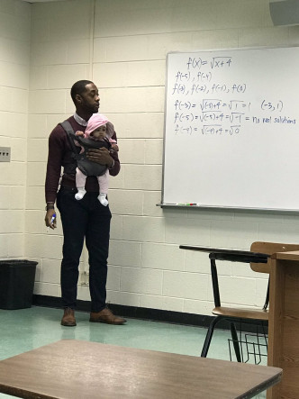亞歷山大一邊緊抱女嬰，一邊拿着筆為學生授課。網圖