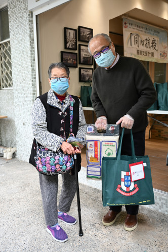 周松崗（右）聯同東華三院的代表，在深水埗白田邨向長者派發口罩等抗疫物資。  政府圖片