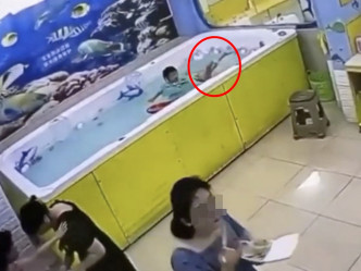 女童母亲背着水池吃饭盒，完全没发现女儿遇溺(红圈)。影片截图
