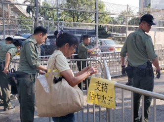 一名女子下午将手持的「支持占中九子」黄色纸张贴在收押所外的铁马上。