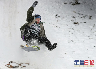 有人苦中作樂在雪地上玩滑雪板。AP圖片