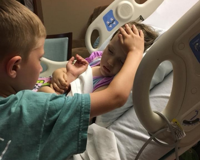 6岁哥哥Jackson站在病床边，注视着与病魔搏斗的妹妹，右手轻抚上她的前额，画面令人动容。