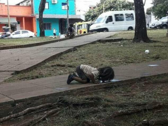 一張小女孩跪地啜飲路邊積水，引發大眾關注當地貧窮問題。（互聯網圖片）