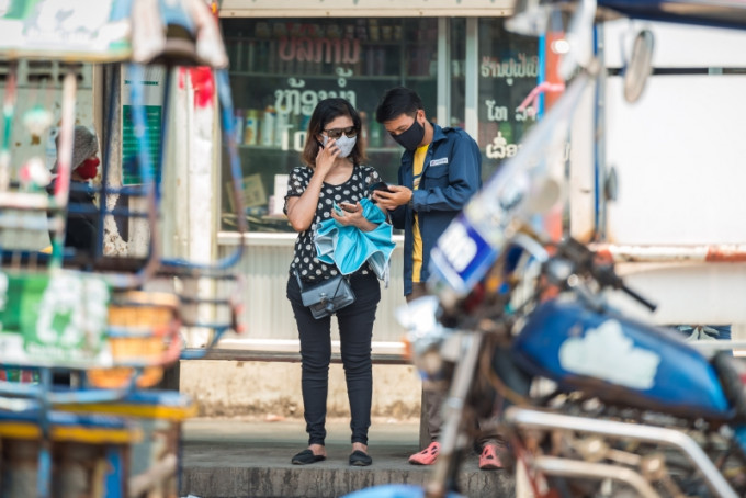 老挝万象街头，市民戴口罩交谈。(新华社)