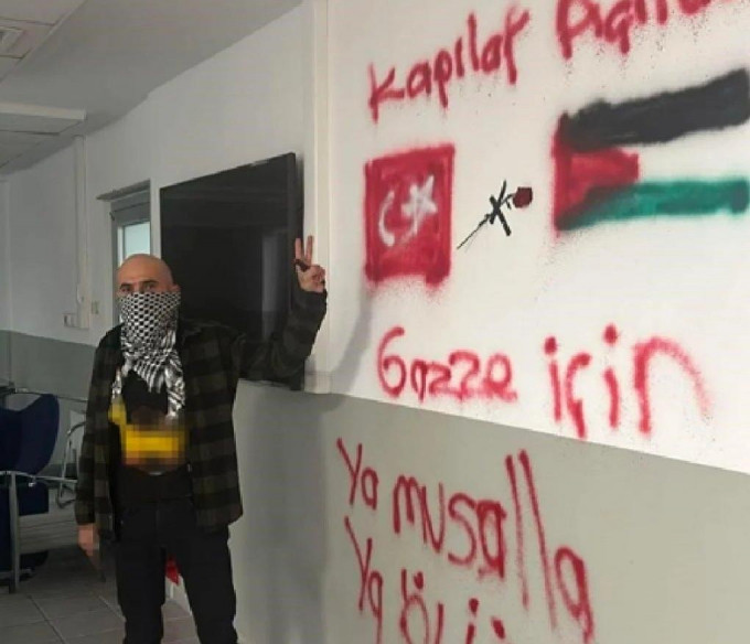 槍手臉上蒙著黑白巴勒斯坦頭巾，舉起V字手勢，背後牆上畫了土耳其及巴勒斯坦國旗。網上圖片