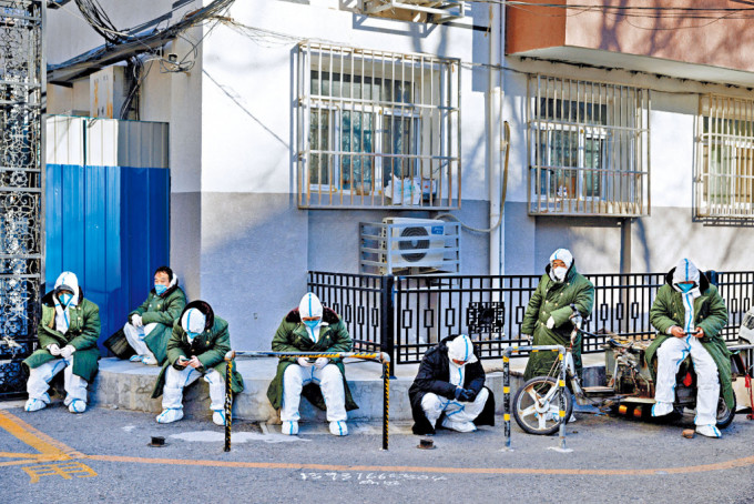 北京疫情持續，不少防疫人員在街頭蹲坐休息。