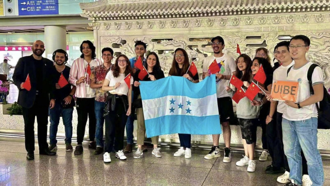 刚刚抵达首都国际机场的洪都拉斯留学生在机场手举五星红旗和洪都拉斯国旗合影留念。UIBE为对外经贸大学英文缩写。 央视截图