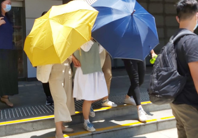 被告刘晓敏（绿白色衫）早前在伞阵下离开法院。 资料图片
