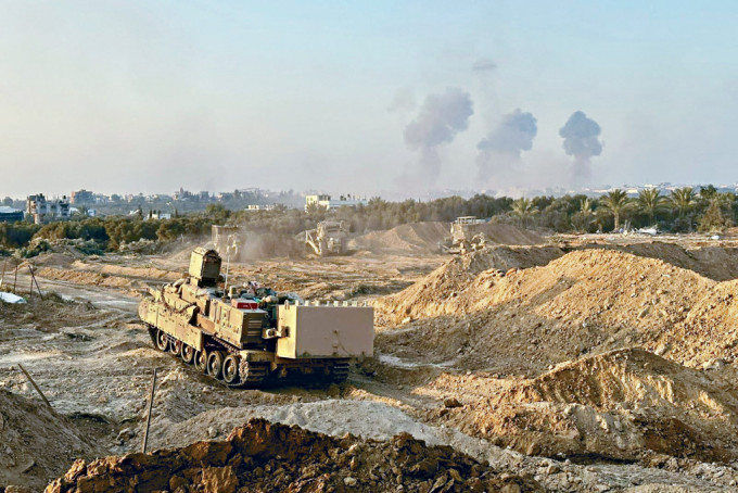 以軍裝甲車在加沙地帶推進，遠處可見硝煙升起。