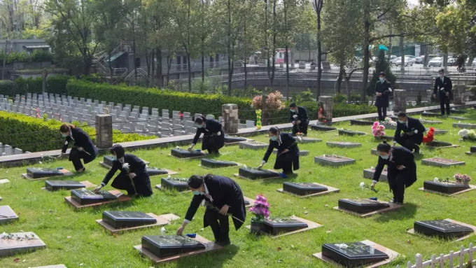 2022年清明期间由工作人员代家属在墓碑前献花鞠躬。新华社图