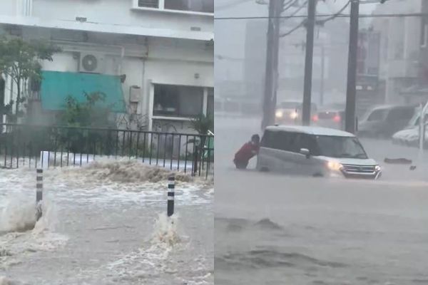 沖繩破紀錄大雨水淹大腿，民眾涉水推車。X圖片