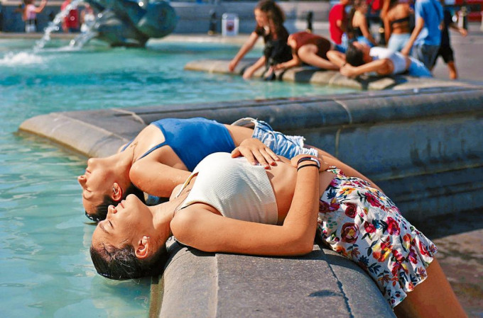 在伦敦特拉法加广场，两名女子把头浸在喷泉消暑。