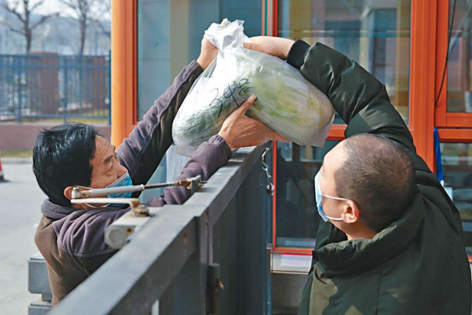 ■西安一小区居民接过配送的蔬菜。