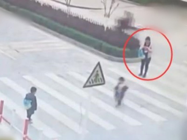 两名孩子在马路上来回奔跑，该名母亲却只顾玩手机。 网图