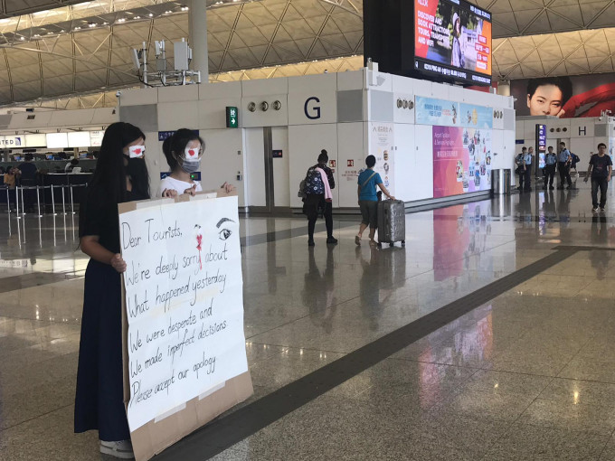 兩名右眼貼染紅紗布的示威者在禁區外向旅客說對不起。