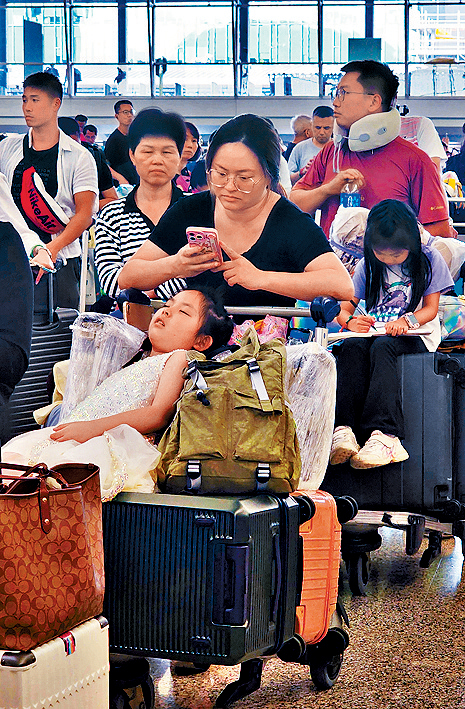 大批旅客在机场等候办理登机，有小童直接睡在行李上。