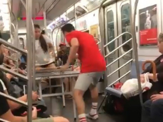 美國紐約一對情侶在地鐵內打起乒乓球，吸引不少乘客目光。(網圖)