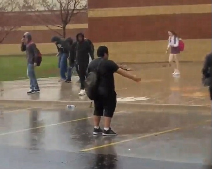 片段中一名男學生雨中動也不動地站着，面向着校舍。網圖