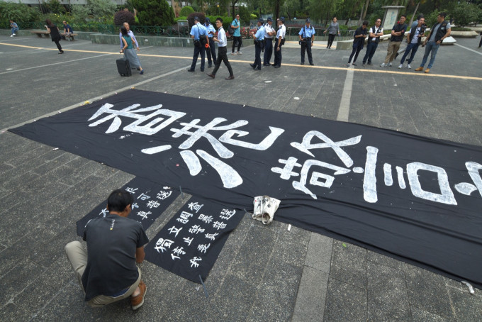 有参加者在地上展示一幅黑底白字直幡。