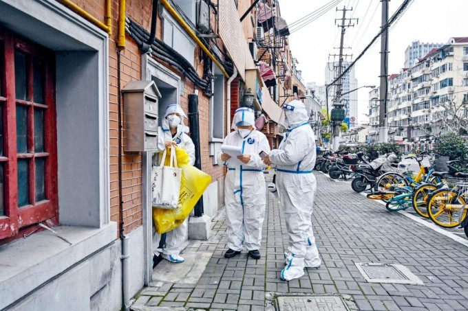 上海感染人數上升，政府推「核酸加自測」篩查工作。身穿防護服的社區工作人員上門派發檢測包。