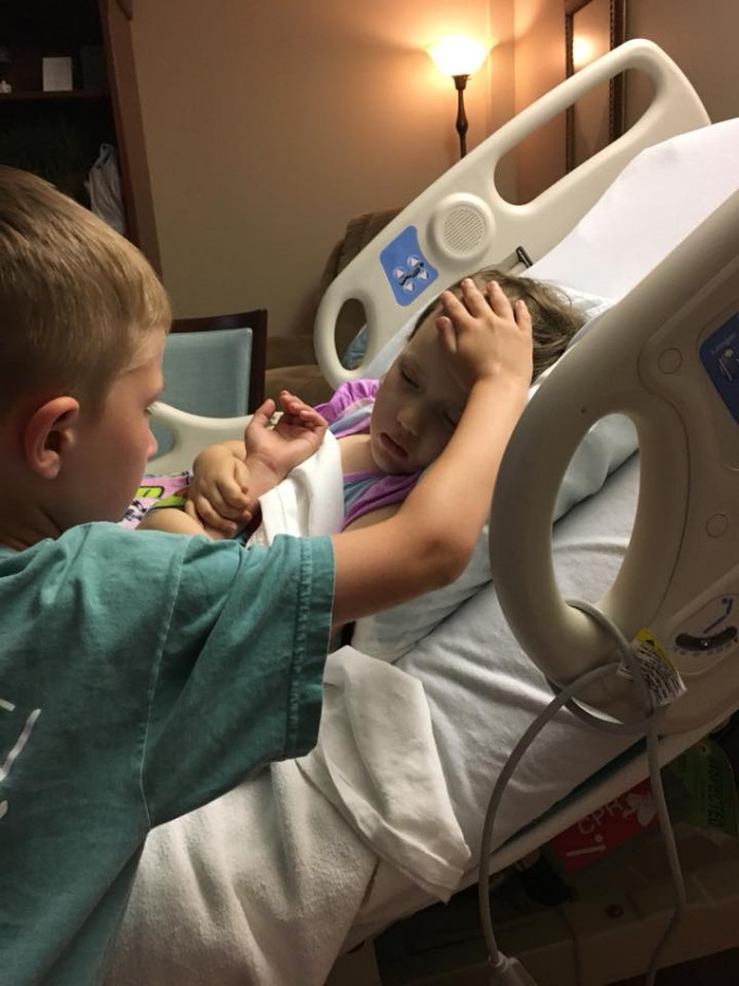 6岁哥哥Jackson站在病床边，注视着与病魔搏斗的妹妹，右手轻抚上她的前额，画面令人动容。