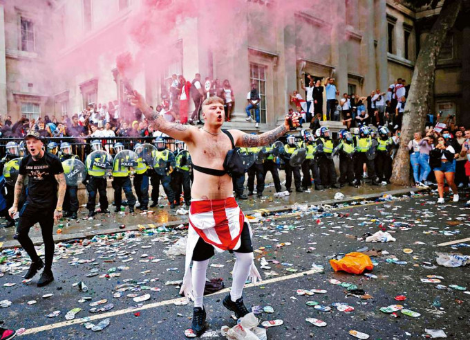 在倫敦特拉法加廣場，一名英格蘭球迷周日在警察防綫前揮動煙霧彈。　