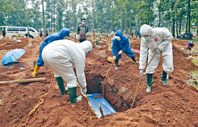 印尼西爪哇的工人穿着防护服掘穴，埋葬病人遗体。