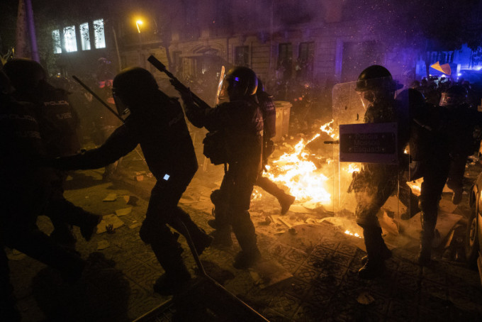 西班牙防暴警察在與巴塞羅那的抗議者發生衝突時越過燃燒的障礙。AP
