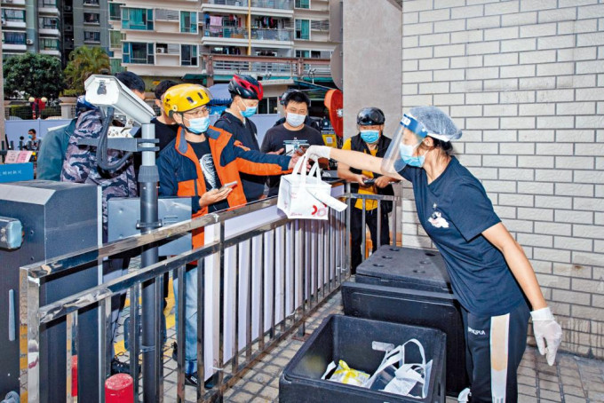 深圳一隔离区的蛋糕店职员，隔着围栏将外卖定单的货品交给快递员。
